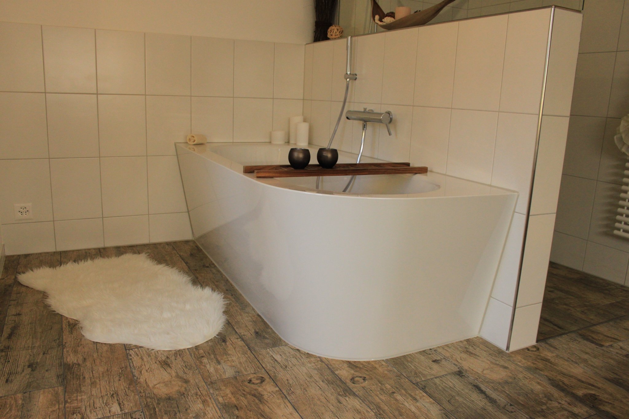 Freistehende Badewanne vor weissen Wandplatten, Boden in Holzoptik
